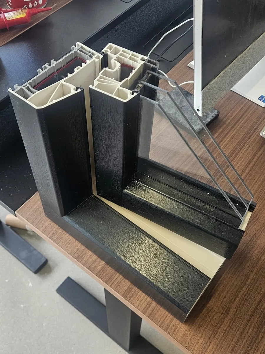 Doorgezaagd zwart kunststof kozijn met driedubbel glas, de drie ruiten en twee spouwen zijn zichtbaar